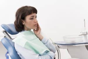 Femeie care ține mâna la obraz din cauza durerii provocate de o măsea de minte care erupe incorect