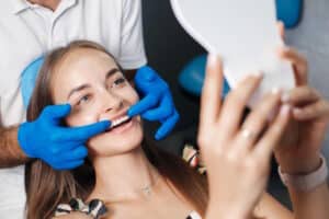 Femeie pe scaunul dentistului privind dintii in oglinda