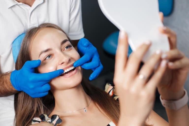Femeie pe scaunul dentistului privind dintii in oglinda