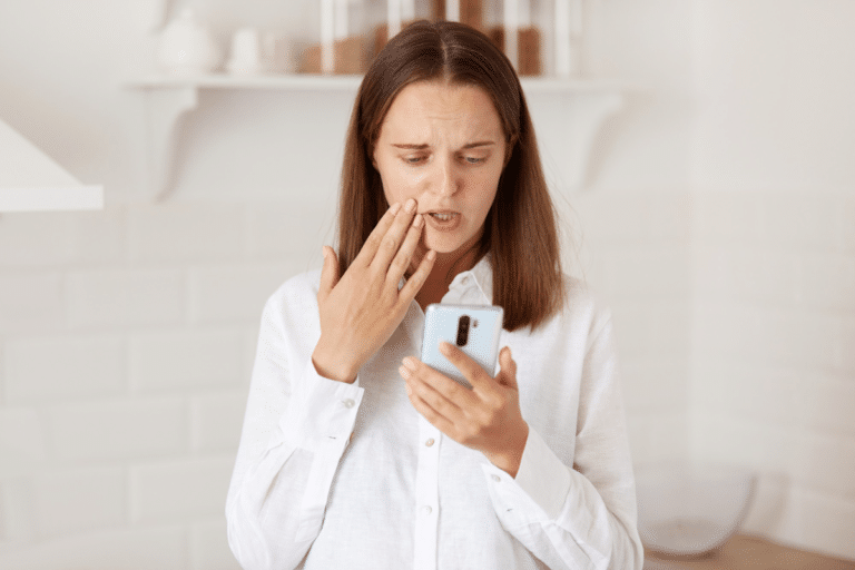 Femeie cu durere de dinti, care se uita pe telefon