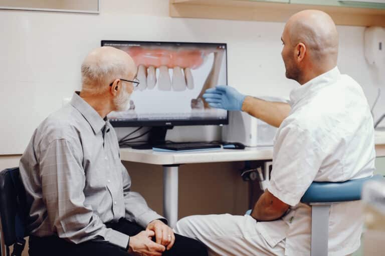Pacient si dentist, in cabinetul dentar, in fata imaginii cu dantura cu parodontoza, inainte de implant dentar